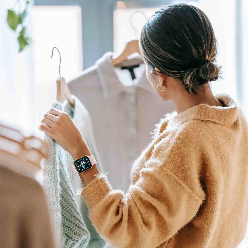 Woman in a beige sweater holding a hanger with a garment, wearing a smartwatch.